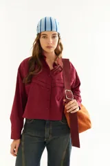 Camisa de corte boxy y calce holgado, color bordó, con cuello clásico, cierre frontal de botones y detalle de tablas con recortes diagonales en el pecho.