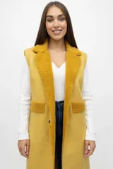 Chaleco largo sin mangas color mostaza, con solapas amplias y detalles en los bolsillos de textura tipo corderito o bucle. Presenta un cierre frontal con un botón y corte recto.
