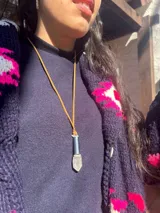 Collar con tiento de cuero y dije compuesto por un tubo metálico y una piedra natural en bruto.