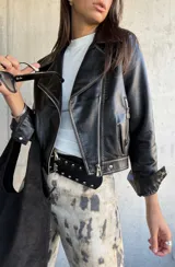 Chaqueta tipo biker de cuero vegano color negro, con solapas amplias, cierre frontal cruzado y detalles de cierres metálicos en los bolsillos y puños.