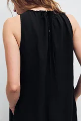 Vestido midi de color marrón con acabado satinado, cuello redondo con detalle fruncido y diseño sin mangas. Presenta un corte fluido con bajo asimétrico y bolsillos laterales ocultos.