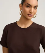 Blusa fucsia de manga corta con cuello redondo pespunteado, diseño sin estampa y efecto airflow con textura sutil. Cuenta con abertura trasera tipo gota y cierre con botón.