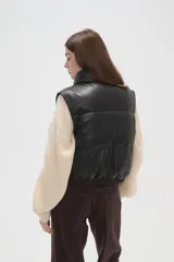 Chaleco acolchado de cuero sintético en color negro, con cuello alto, cierre frontal con botones a presión y diseño sin mangas.