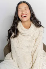 Sweater tipo poncho color crudo, tejido en punto grueso con cuello alto y mangas largas amplias.