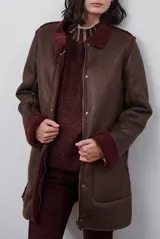 Chaquetón de efecto cuero en color marrón, con interior y detalles en corderito color bordó. Presenta cierre frontal con cremallera y botones a presión, cuello solapa y mangas largas con puños de corderito.