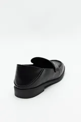 Mocasín de cuero sintético negro con punta cuadrada, detalle de costuras visibles en la capellada y taco bajo.
