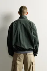 Cazadora relaxed fit de denim de algodón color verde oscuro, con cuello subido y cierre de cremallera frontal. Cuenta con bolsillos de vivo con solapa en la cadera, acabados elásticos y detalle bordado a contraste en el pecho.