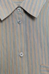 Camisa fluida de corte oversize confeccionada en mezcla de viscosa, con diseño de rayas verticales finas en tono beige sobre fondo blanco. Presenta cuello solapa, cierre frontal con botones, manga larga con puños y un bolsillo de plastrón en el pecho.