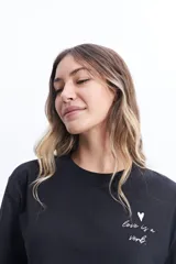 Remera corta (cropped) de algodón color verde lima, con cuello redondo y manga corta. Presenta un pequeño estampado en el pecho con un corazón naranja y texto manuscrito.