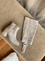 Botas de caña alta desmontables que se transforman en botinetas, confeccionadas en gamuza color beige. Presentan un diseño de punta semicuaadrada, taco cuadrado de 6 cm y detalle de estribo con hebilla forrada en el tobillo.