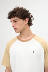 Remera estilo raglán color blanco en el cuerpo con mangas cortas color arena y cuello redondo marrón. Presenta un pequeño bordado en el pecho.