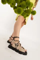 Sandalias bajas color beige con estampado de reptil, tiras finas negras para atar al tobillo y suela track negra.