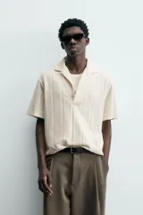 Polo de hombre color crema, de tejido texturado con rayas verticales en relieve, corte relajado, cuello bowling y cierre frontal parcial con botones.