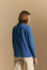 Blusa de algodón color azul con textura bordada, cuello con volado y cierre frontal con botones. Presenta mangas largas y un calce relajado.