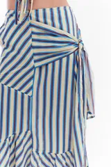Falda midi confeccionada en algodón y lino con diseño de rayas verticales en tonos amarillo, azul y rojo. Presenta recortes diagonales y un lazo lateral para atar en la cintura, con detalle de volados en el ruedo.