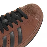 Championes Adidas modelo Superstar II, confeccionados en gamuza color marrón con las icónicas tres tiras laterales en cuero negro. Presenta la clásica puntera de goma texturizada, lengüeta negra y suela de goma al tono.