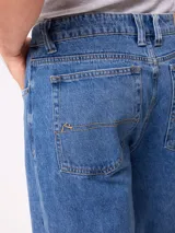 Jean de corte slouchy fit, confeccionado en denim de algodón color azul medio. Presenta diseño de cinco bolsillos, cierre frontal con botón y costuras reforzadas en tono contrastante.