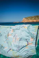 Short de baño color celeste con estampado botánico de hojas y flores en tonos verdes, naranjas y violetas. Cuenta con cintura elástica, bolsillos laterales y un bolsillo trasero con etiqueta de la marca.