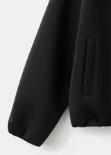 Chaqueta negra de diseño estructurado, con cuello alto, cierre frontal de cremallera metálica y mangas abullonadas con puños ajustados.