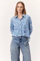 Camisa de corte oversize con diseño a rayas verticales en color azul y blanco, cuello camisero, mangas largas y bolsillos frontales con solapa.