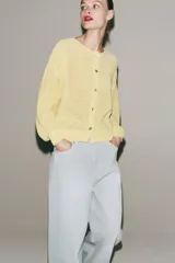 Chaqueta de punto rústico color amarillo claro, con cuello redondo, manga larga y cierre frontal con botones nacarados.