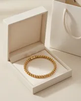 Pulsera esclava de acero con baño de oro, compuesta por pequeñas esferas metálicas unidas en un diseño elástico.