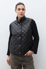Chaleco acolchado reversible con diseño capitoneado romboidal y cuello alto. Cuenta con cierre frontal de botones a presión.