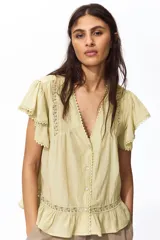 Blusa de tejido liviano color amarillo claro, con escote en V profundo, mangas cortas estilo mariposa y cierre frontal con botones. Presenta detalles de alforzas e inserciones de encaje en el frente y en el borde del ruedo y las mangas, terminando en un volante inferior.
