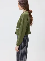 Cardigan de algodón grueso color rojo, con cuello redondo, cierre frontal de botones grandes y bolsillos cuadrados en el frente. Presenta detalles de pelo sintético en el cuello y los bolsillos, y logo bordado en uno de los bolsillos.