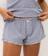 Pijama short doll de dos piezas confeccionado en algodón, con estampa de cuadros vichy en tonos azul y blanco. La musculosa presenta breteles finos, escote corazón con delicado encaje blanco y silueta fluida. El short cuenta con cintura elástica, pequeño moño frontal y terminación ondulada en el ruedo.