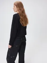 Cardigan de algodón grueso en color rojo, con cuello redondo y cierre frontal de botones grandes. Presenta bolsillos cuadrados en el bajo con detalles de pelo sintético en los bordes y logo bordado en uno de ellos. Posee puños y ruedo elastizados con diseño holgado.