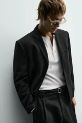 Blazer de corte cropped confeccionado en tejido con viscosa, color negro. Presenta cuello con solapas de muesca, cierre frontal de tres botones, mangas largas con puños abotonados y bolsillos de vivo en la cadera.