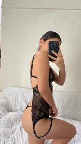Conjunto de lencería de cuatro piezas en encaje negro, compuesto por un bralette con cierre frontal, una pieza tipo chaleco con portaligas integrado y una tanga colaless. Incluye ligas regulables.