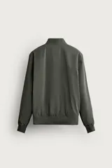 Cazadora bomber de tejido técnico ligero color marrón oscuro, con corte regular fit, cuello, puños y ruedo de rib elástico, bolsillos frontales de vivo y cierre frontal con cremallera.