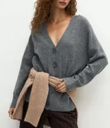 Cardigan de punto color beige con escote en V, cierre frontal con botones grandes y mangas largas con puños acanalados. Presenta un corte recto y estructurado.