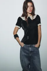 Camisa de terciopelo negro con cuello solapa grande en crochet color crema y detalles de crochet en los bordes de las mangas cortas. Presenta un diseño entallado con cierre de cremallera en la espalda.