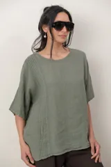 Blusa de lino color marrón oscuro, con escote redondo, mangas cortas amplias y detalle de alforzas verticales en el lateral derecho.