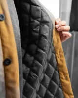 Sobre camisa negra de pana con cuello clásico, cierre frontal con botones, dos bolsillos con solapa abotonada en el pecho y puños abotonados. Interior acolchado con patrón de rombos.