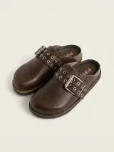 Zueco de cuero color chocolate, con diseño de punta redondeada y tira ajustable sobre el empeine con hebilla metálica y detalle de ojales decorativos.