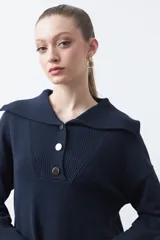 Sweater de tejido de punto color azul marino, con cuello polo amplio y cierre frontal con tres botones metálicos. Presenta mangas largas levemente acampanadas y un diseño de silueta relajada con aberturas laterales en el ruedo.