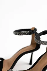 Sandalias de tacón alto negras con tiras adornadas con pedrería brillante. Tienen una tira en la parte delantera del pie y otra alrededor del tobillo con cierre de cremallera en la parte trasera.