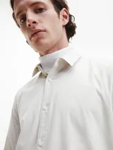 Camisa de manga larga color blanco hueso, de corte slim, con cuello tradicional y cierre frontal de botones.