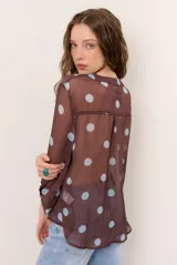 Blusa marrón semitransparente con estampado de lunares celestes, mangas largas abuchonadas, cuello en V con lazos y detalles de volados frontales.