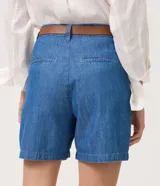 Short de sastrería confeccionado en jean azul de algodón, con cintura alta, pinzas delanteras, bolsillos laterales y presillas. Incluye un cinturón delgado de cuero marrón con hebilla metálica.