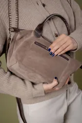 Cartera tipo bolso de mano confeccionada en cuero gamuzado color suela, con solapa de cuero liso y cierre metálico. Incluye doble manija corta y correa larga desmontable.