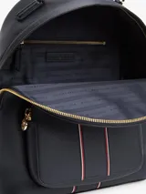 Mochila de poliuretano texturizado en color azul marino, con diseño curvo, bolsillo frontal con cierre y detalles de franjas verticales con los colores distintivos de la marca. Cuenta con el monograma TH metálico en dorado, cierre de cremallera superior, asa de mano y correas ajustables para la espalda.