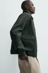 Cazadora relaxed fit color verde oscuro, confeccionada en tejido de algodón. Cuenta con cuello solapa, manga larga con puño abotonado, bolsillos plastrón con solapa en la cadera y cierre frontal de botonadura.