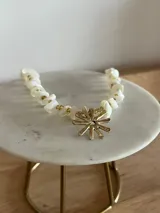 Gargantilla artesanal compuesta por piedras naturales blancas irregulares intercaladas con pequeñas cuentas doradas. Presenta un dije central en forma de sol de bronce y cuenta con cadena de alargue con cierre de mosquetón.