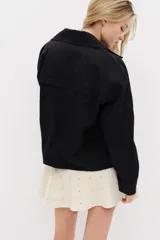 Chaqueta negra de corte relajado confeccionada en mezcla de algodón y lyocell, con solapas anchas redondeadas, hombros caídos, botonadura frontal y bolsillos delanteros de parche.