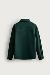 Sobrecamisa de ajuste relajado en color azul marino, con cuello de solapa, manga larga con puño abotonado y cierre frontal con botones. Presenta bordados contrastantes en el frente con la inscripción "St. Louis Worldwide Goods" en tonos naranja y blanco.